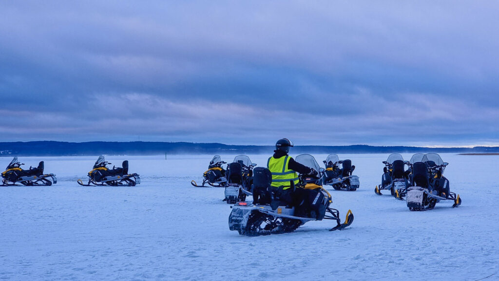 Snowmobiles and a guide on a frozen lake in Vuokatti